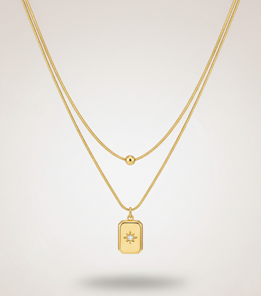 Gold necklace with a rectangular pendant on a light gray background