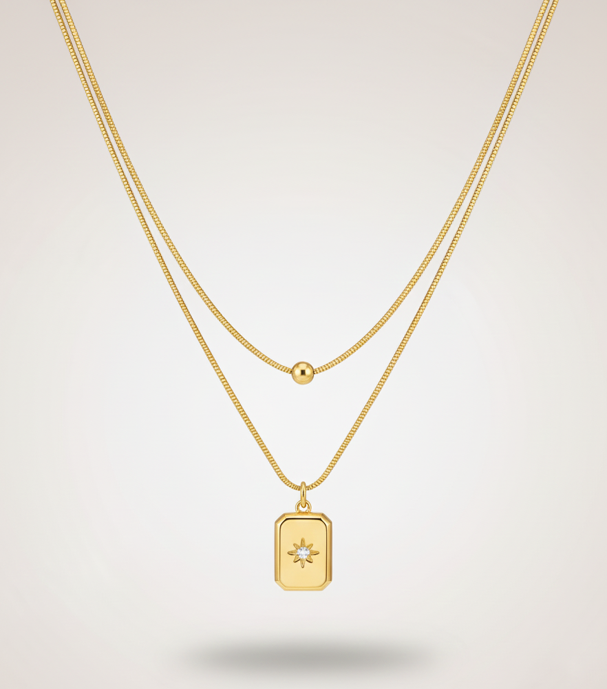 Gold necklace with a rectangular pendant on a light gray background