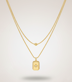 Gold necklace with a rectangular pendant on a light gray background
