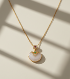 Gold necklace with a white pendant on a beige background