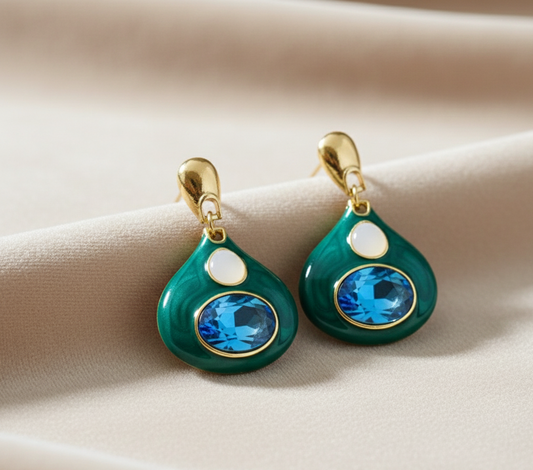 Pair of green teardrop earrings with blue gemstones on a beige fabric background