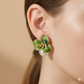Green floral earring with pearl and gemstones worn by a person on a beige background